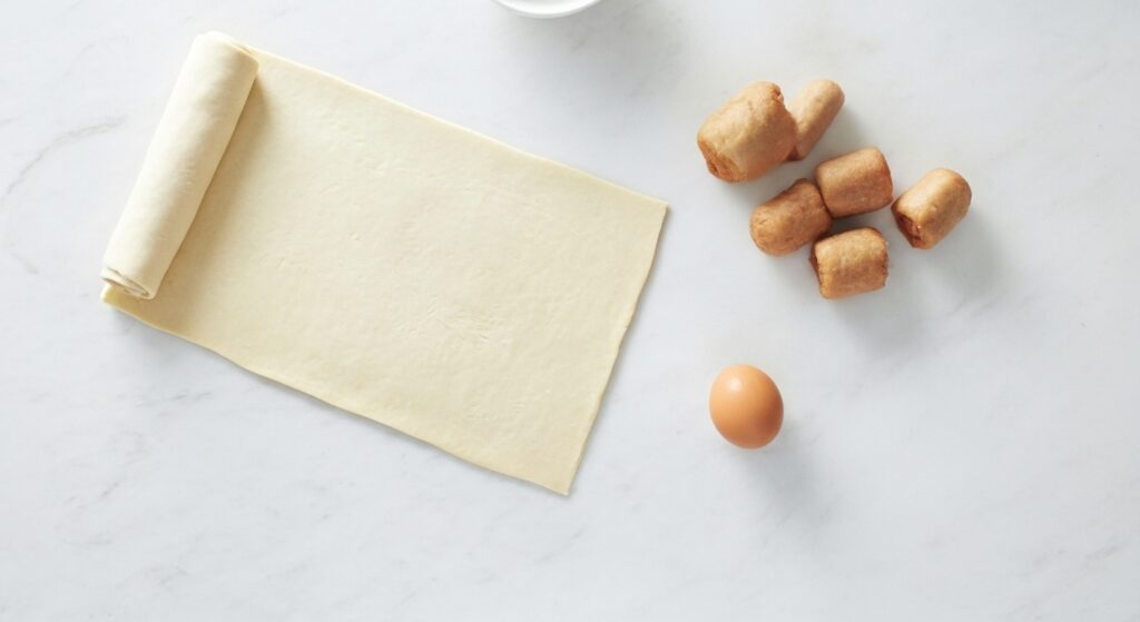 Ingredientes para a receita de enroladinho de salsicha com massa de pastel organizados em uma bancada.